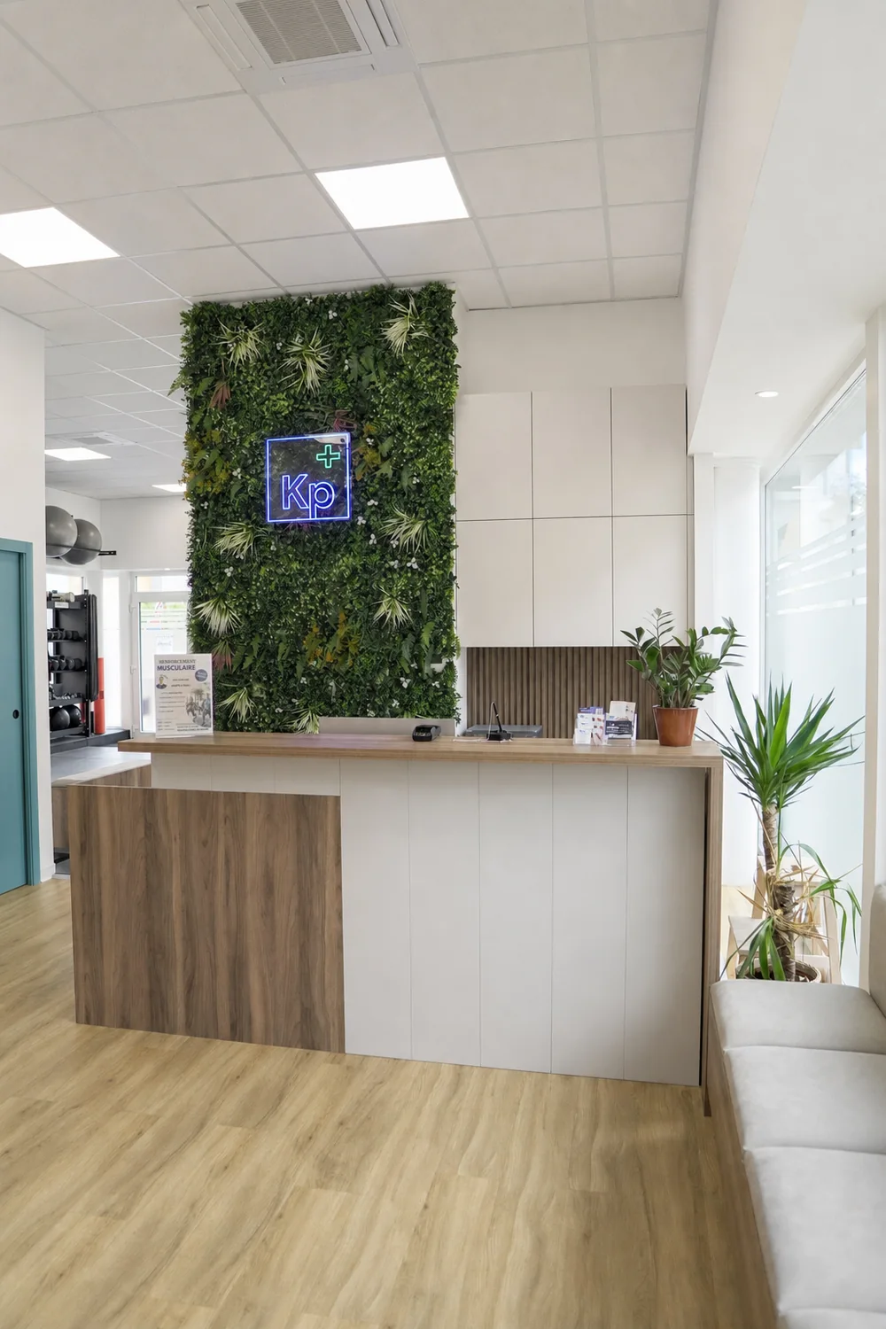 Accueil du cabinet de kiné de Strasbourg : banque d’accueil en bois, mur végétal et enseigne lumineuse