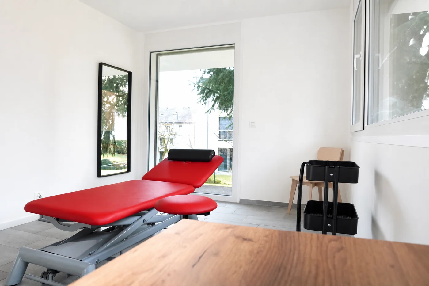 Salle de soin du cabinet de Saint-Sulpice : table rouge, grande baie vitrée sur le jardin